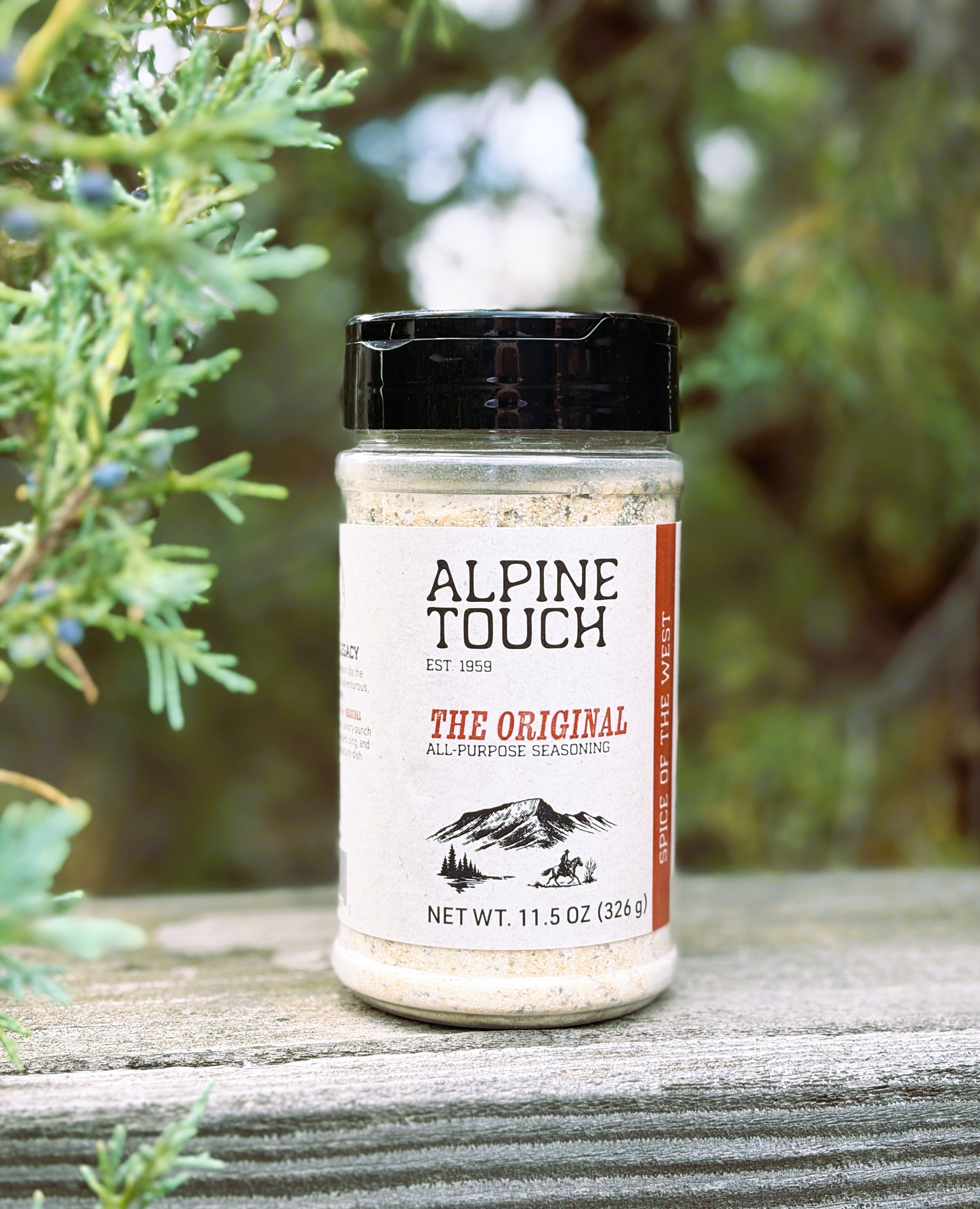 A bottle of Alpine Touch The Original All-Purpose Seasoning placed on a weathered wooden surface with green foliage in the background.