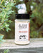 A bottle of Alpine Touch The Original All-Purpose Seasoning placed on a weathered wooden surface with green foliage in the background.