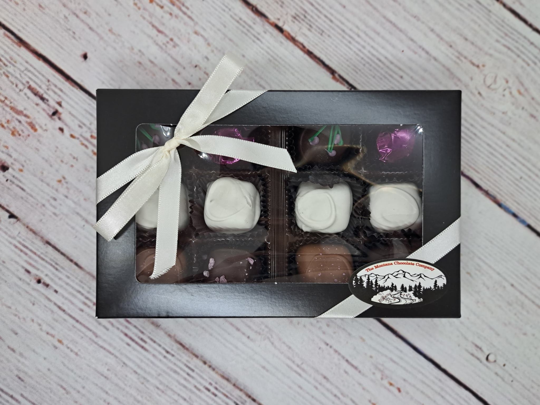 The Montana Chocolate Company Ultimate Huckleberry Box, 12pc Huckleberry Box Includes an equal number milk, dark and white chocolates Hand-crafted in Stevensville, MT 12-piece collection, Black Box with White Ribbon